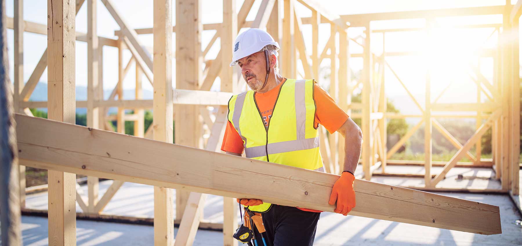 Construction worker carrying a piece of wood inside of a structure of a home.